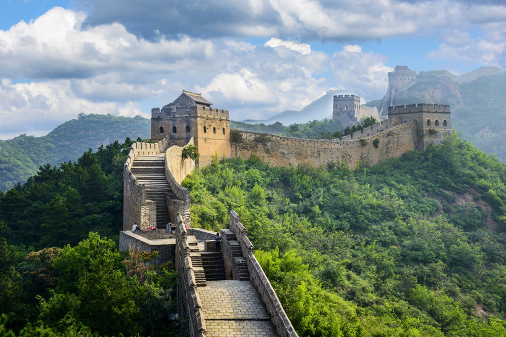 De Chinese Muur slingert over groene bergen onder een blauwe lucht, tijdens een groepsrondreis China.