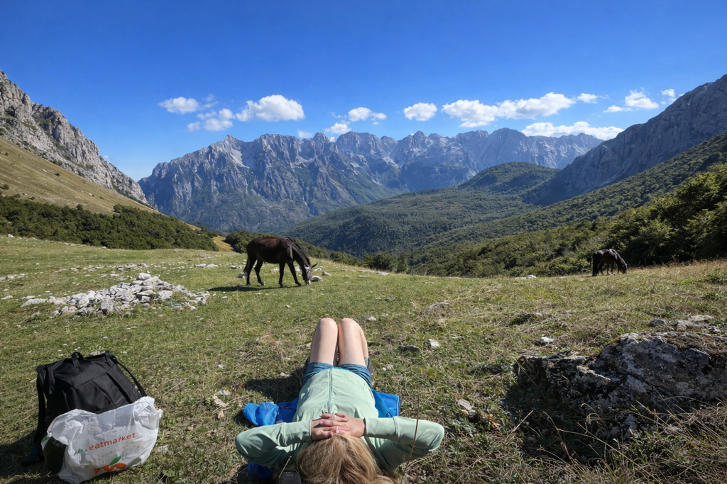 Wandelaar rust uit in bergweide met grazende paarden en uitzicht op Peaks of the Balkan-gebergte.