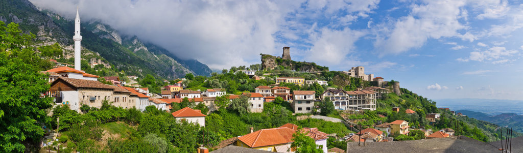 Panorama van Krujë in Albanië met kasteelruïne, moskee en huizen met rode daken in de bergen.