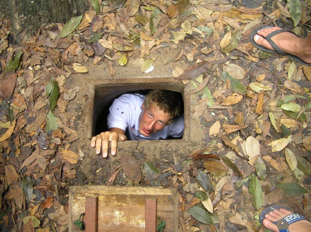 Jongen kruipt uit een smalle tunnel bij de Cu Chi-tunnels tijdens een familiereis Vietnam.