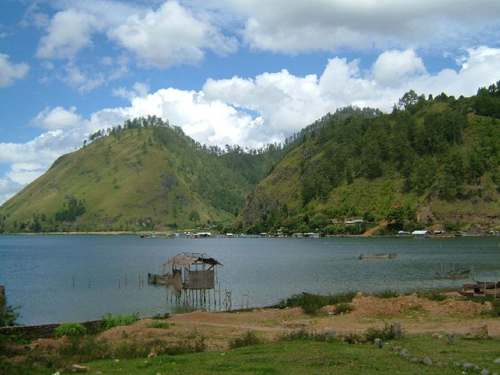 Uitzicht over het Tobameer op Sumatra met groene heuvels en vissershutten op palen onder een blauwe lucht.