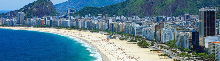 Panoramisch uitzicht op Copacabana-strand in Rio de Janeiro met boulevard, hoogbouw en bergen op de achtergrond.