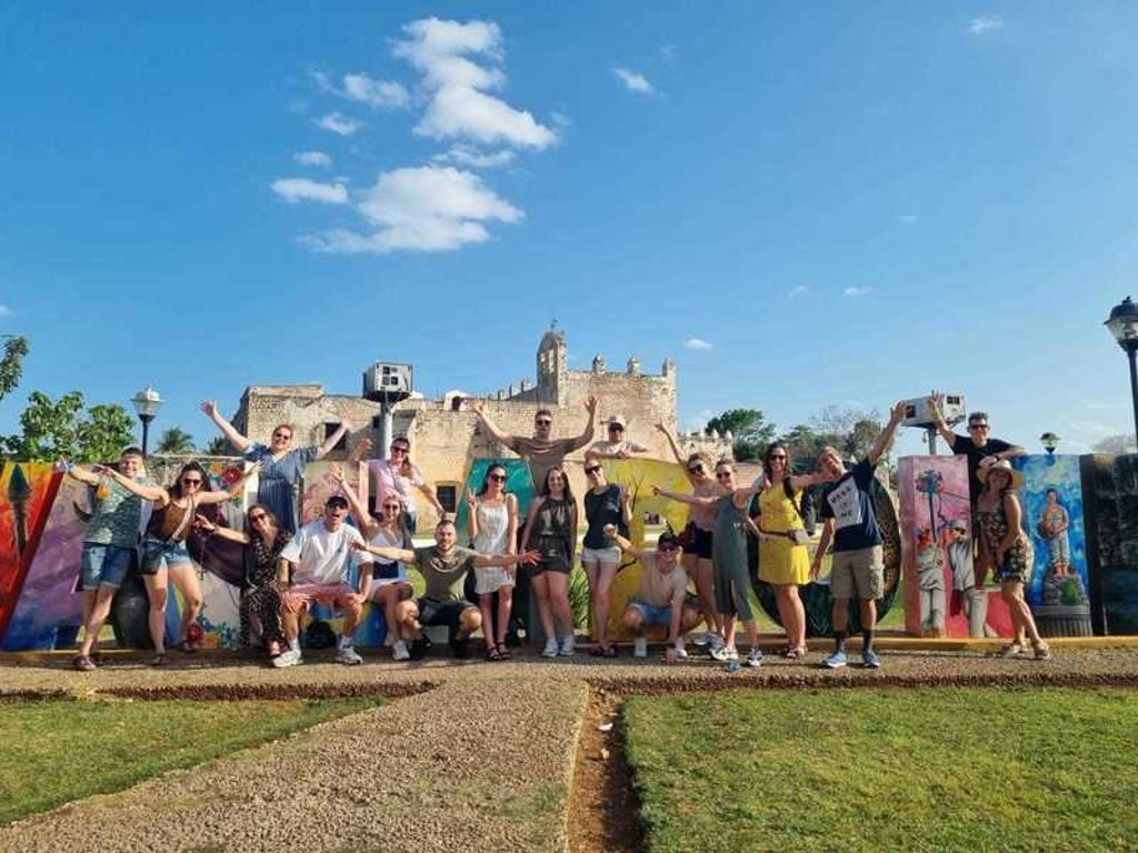Groep reizigers tijdens 22-35ers reis Mexico bij kleurrijke muurschildering en historische ruïnes.