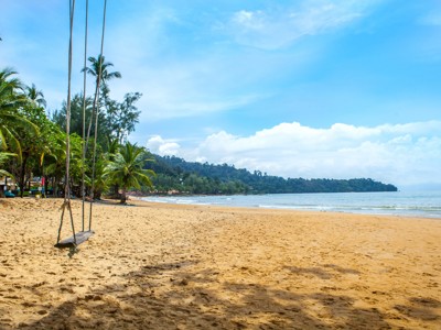 Rustig zandstrand in Zuid-Thailand met palmbomen, zee en een schommel aan touwen.