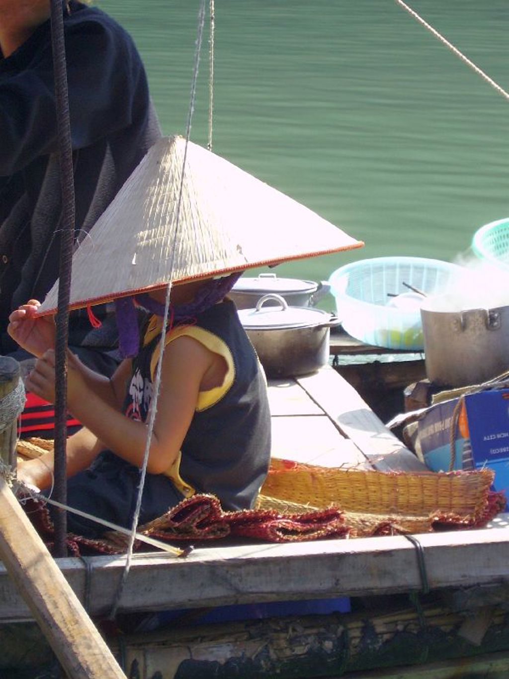 Vrouw met Vietnamese hoed op een boot tussen pannen en manden, tijdens groepsrondreis Vietnam kort.