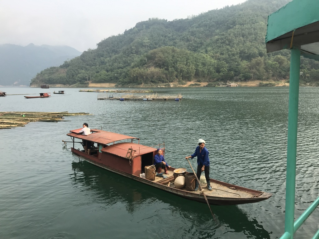 Boot op een meer in Vietnam met twee locals en groene bergen op de achtergrond.