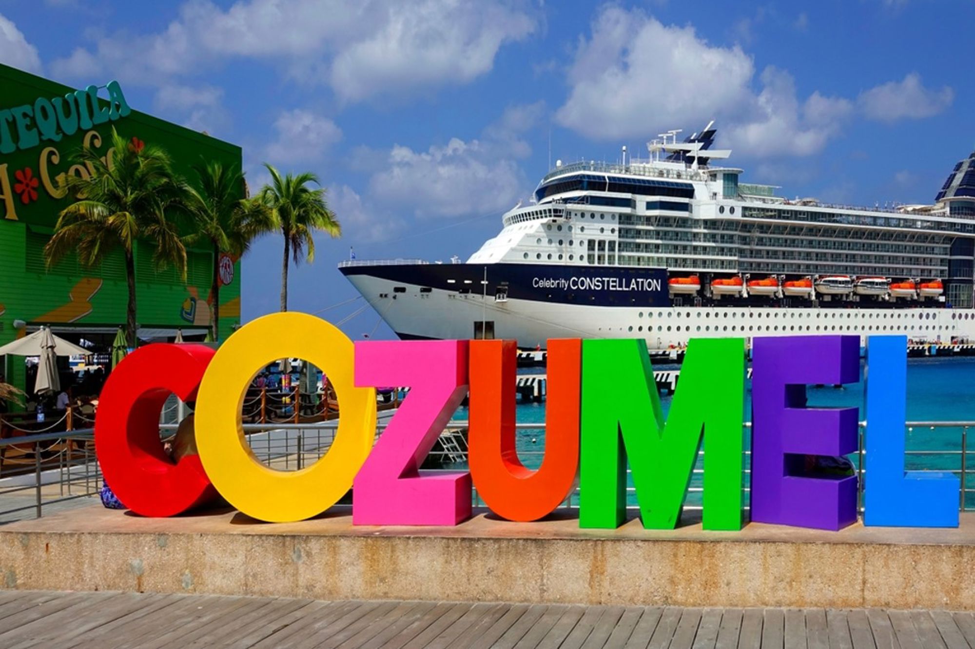 Gekleurde Cozumel-letters bij de cruisehaven, met een groot cruiseschip op de achtergrond.