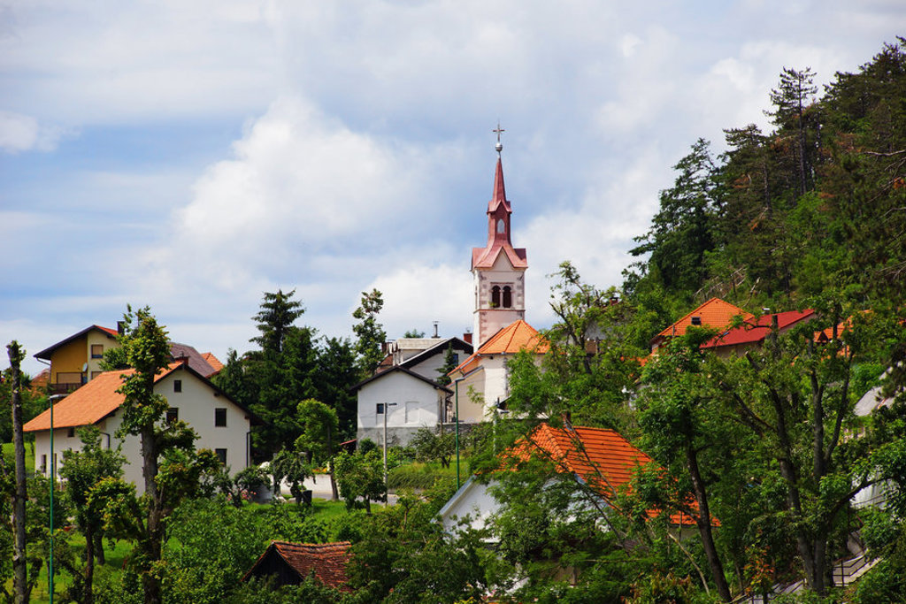 Sloveens dorp met kerktoren en rode daken tussen groen, tijdens een fietsvakantie in Slovenië.