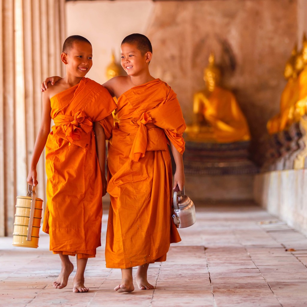 Twee jonge monniken in oranje gewaden lopen door een tempelgang in Laos en Cambodja.