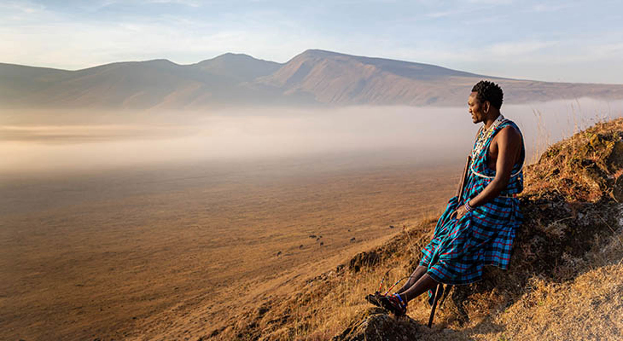 Man in traditionele Maasai-kleding kijkt uit over de Ngorongoro-krater in Tanzania.