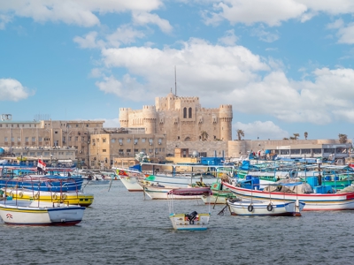Haven van Alexandrië met kleurrijke vissersboten en de Citadel van Qaitbay op de achtergrond.