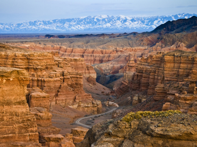 Panorama van de Charyn Canyon met rode rotsformaties en besneeuwde bergen langs de Zijderoute.