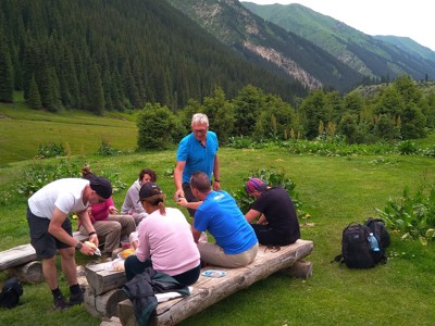Picknickpauze tijdens Route Kirgistan in een groene vallei met naaldbossen en bergen op de achtergrond.