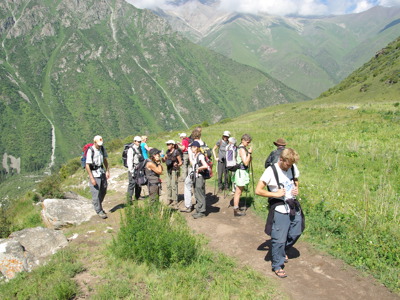 Wandelgroep op bergpad met uitzicht op groene valleien en hoge bergen in Kirgistan.