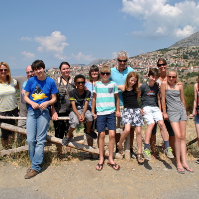 Groep reizigers tijdens familiereis Noord-Griekenland bij uitzichtpunt met bergdorp op de achtergrond.