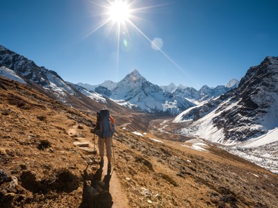 Wandelaar op de Everest Base Camp-route in Nepal, met besneeuwde Himalayatoppen onder een heldere zon.