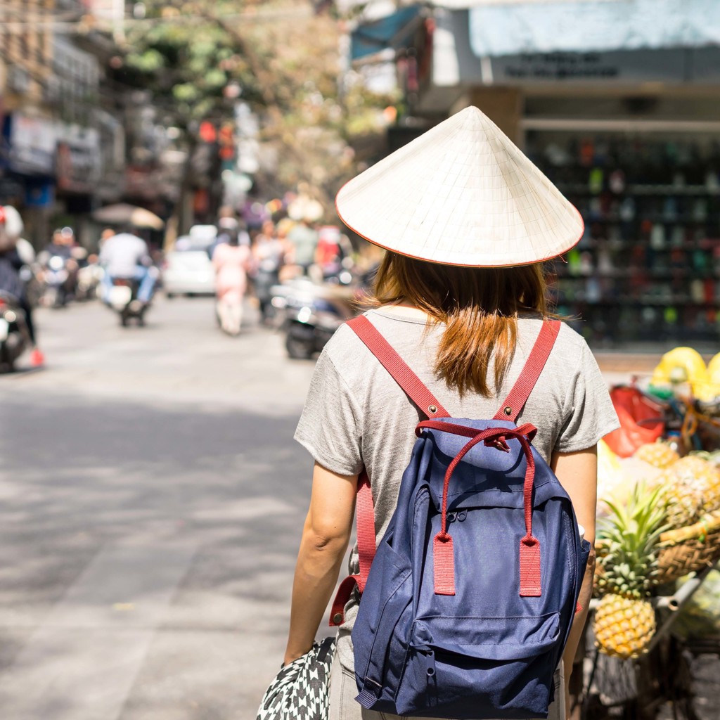 Reiziger met Vietnamese hoed en rugzak loopt door een drukke straatmarkt in Vietnam.