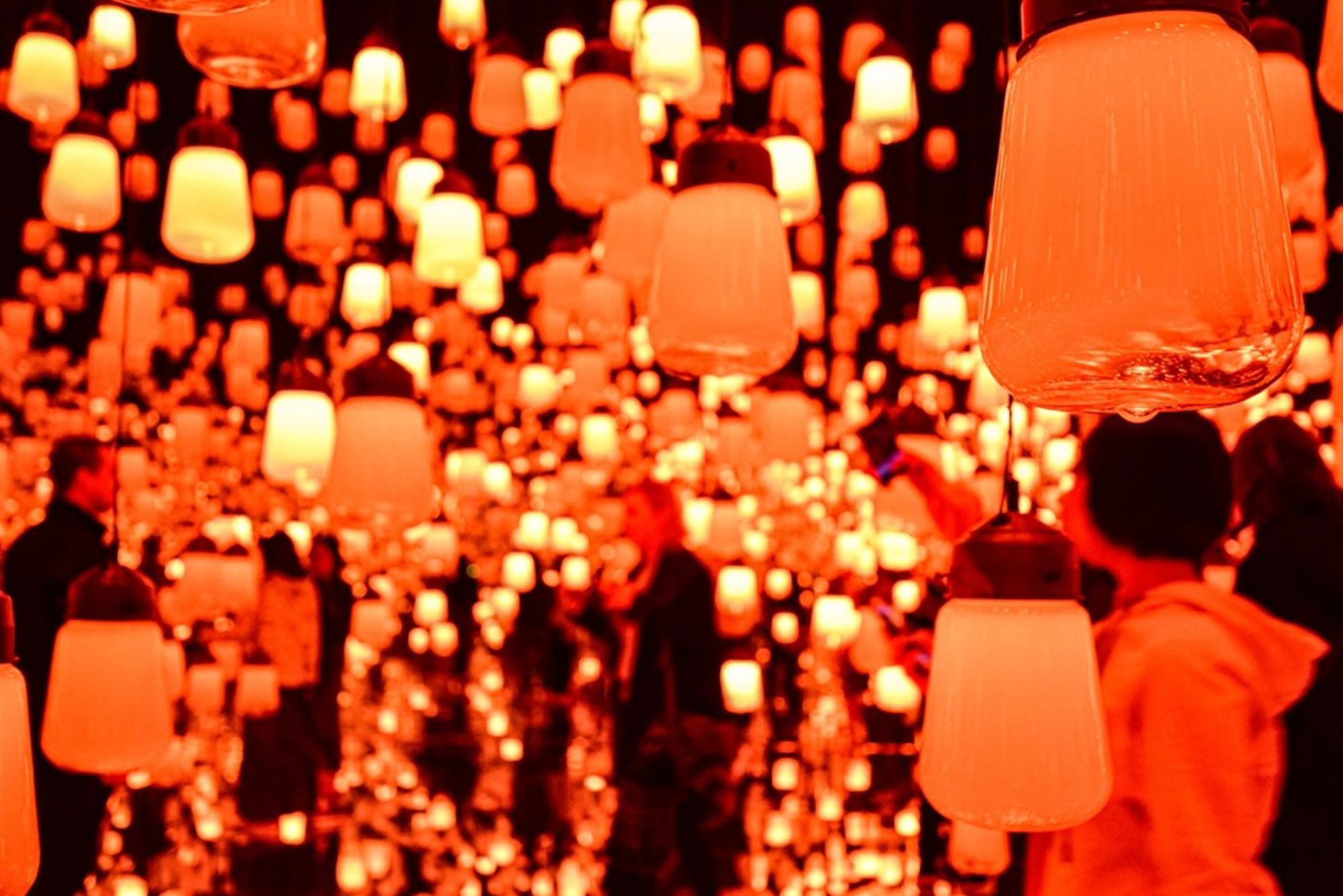 Bezoekers in een Japanse lichtinstallatie met honderden oranje hanglampen.