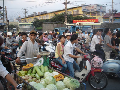 Drukke straat in Vietnam met veel scooters en een groentekraam op een kar.