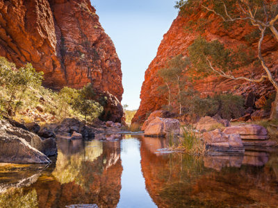 Rode rotswanden en een rustige waterpoel in een kloof in Australië.
