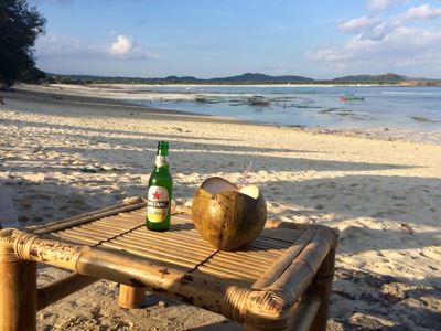 Bamboetafeltje op het strand met een kokosnootdrankje en Bintang-bier, uitkijkend over zee en bootjes op Bali.