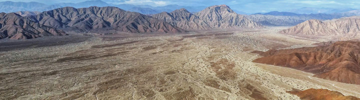 Nazcalijnen in de Nazca-woestijn in Peru, met uitgestrekte vlakte en bergen op de achtergrond.