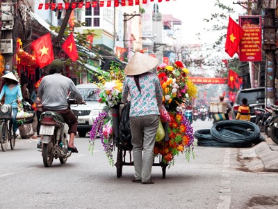 Bloemenverkoper met kar vol kleurrijke boeketten in een drukke straat in Vietnam, met Vietnamese vlaggen.