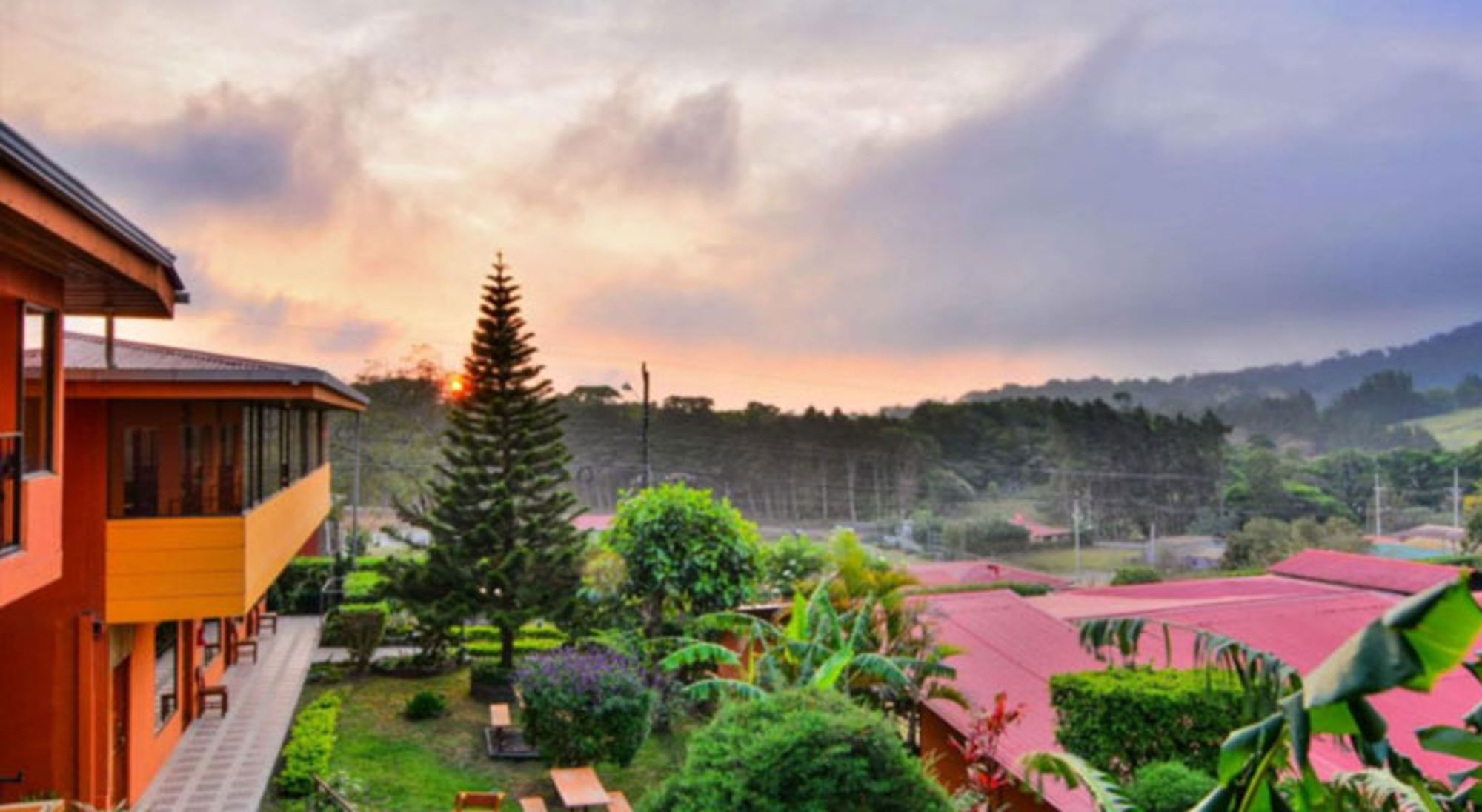 Zonsondergang boven groene heuvels en lodge met tropische tuin in Costa Rica.