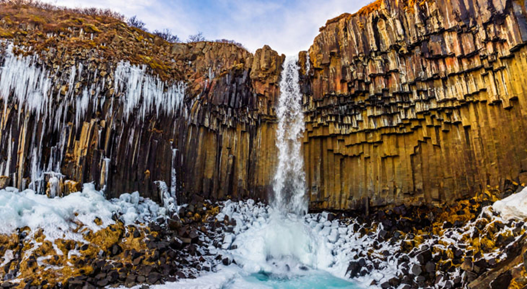 Waterval bij basaltkolommen met ijs en sneeuw in IJsland.