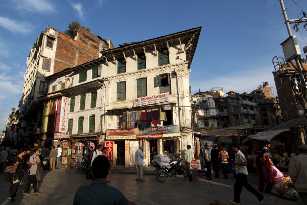 Drukke straatmarkt in Kathmandu met winkels en traditioneel gebouw, tijdens groepsrondreis Tibet en Nepal.