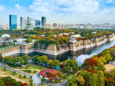 Osaka Castle met gracht en herfstkleuren, met skyline van Osaka op de achtergrond.