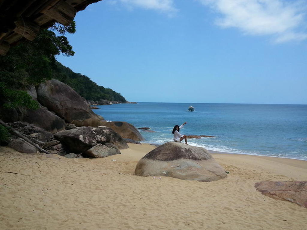 Rotsachtig strand aan de Braziliaanse kust met een reiziger op een rots en een boot op zee.