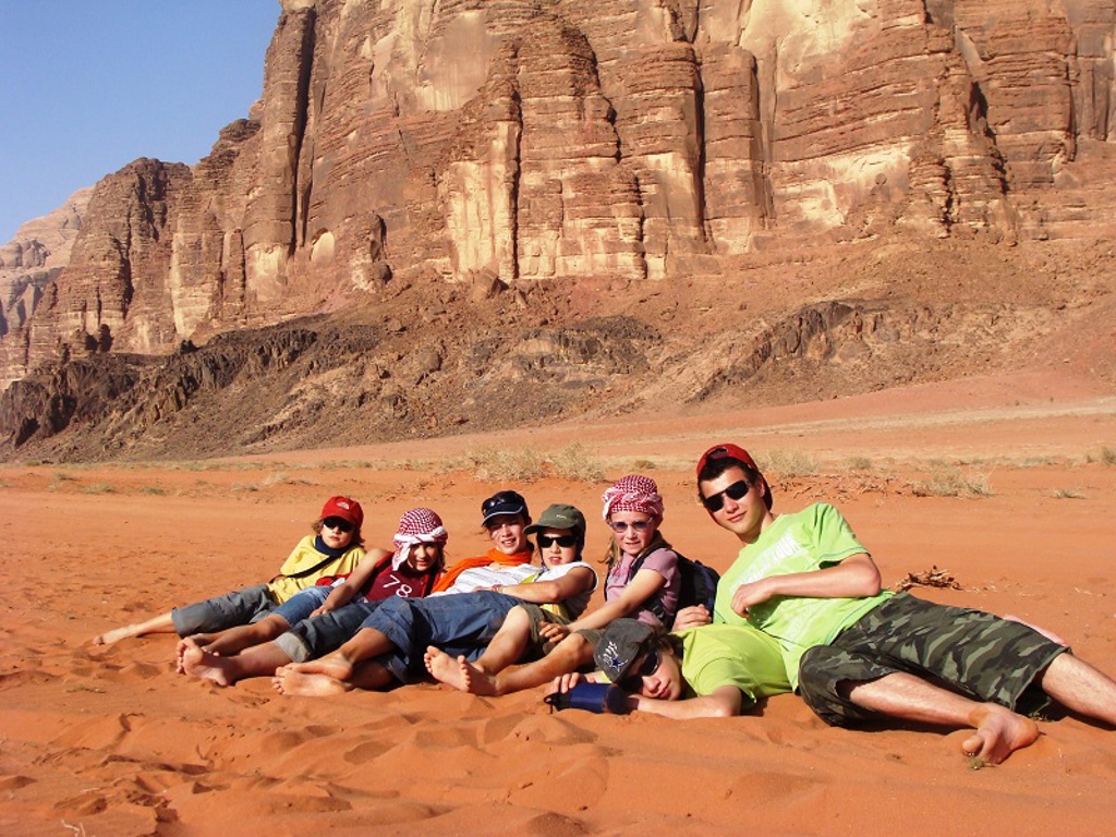 Gezin ontspant in het zand van Wadi Rum in Jordanië, met rotsformaties op de achtergrond.