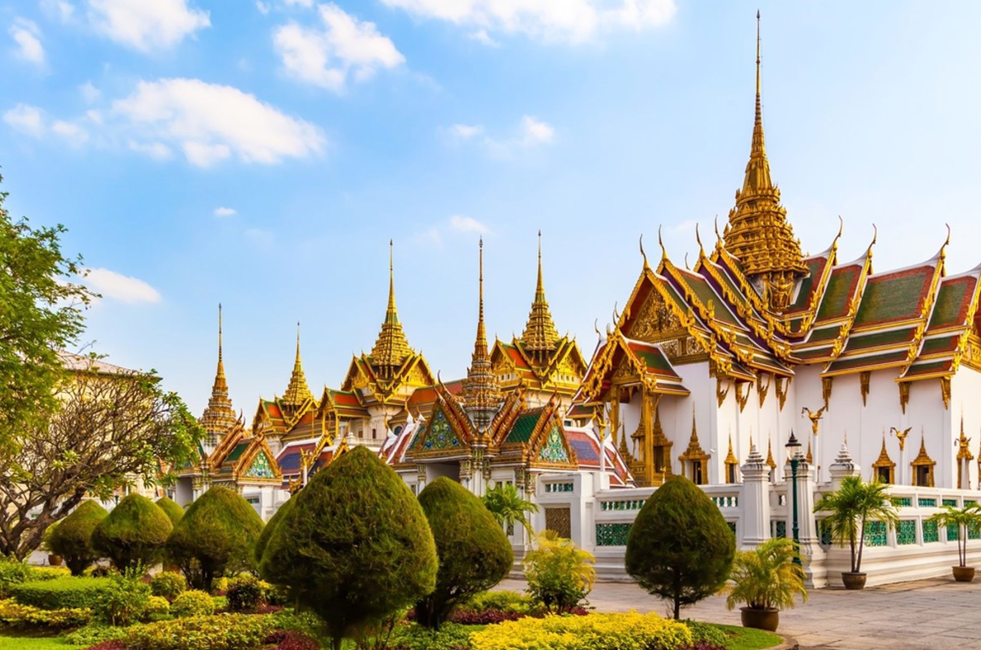Het Grand Palace in Bangkok met gouden tempeldaken en pagodes onder een blauwe lucht.
