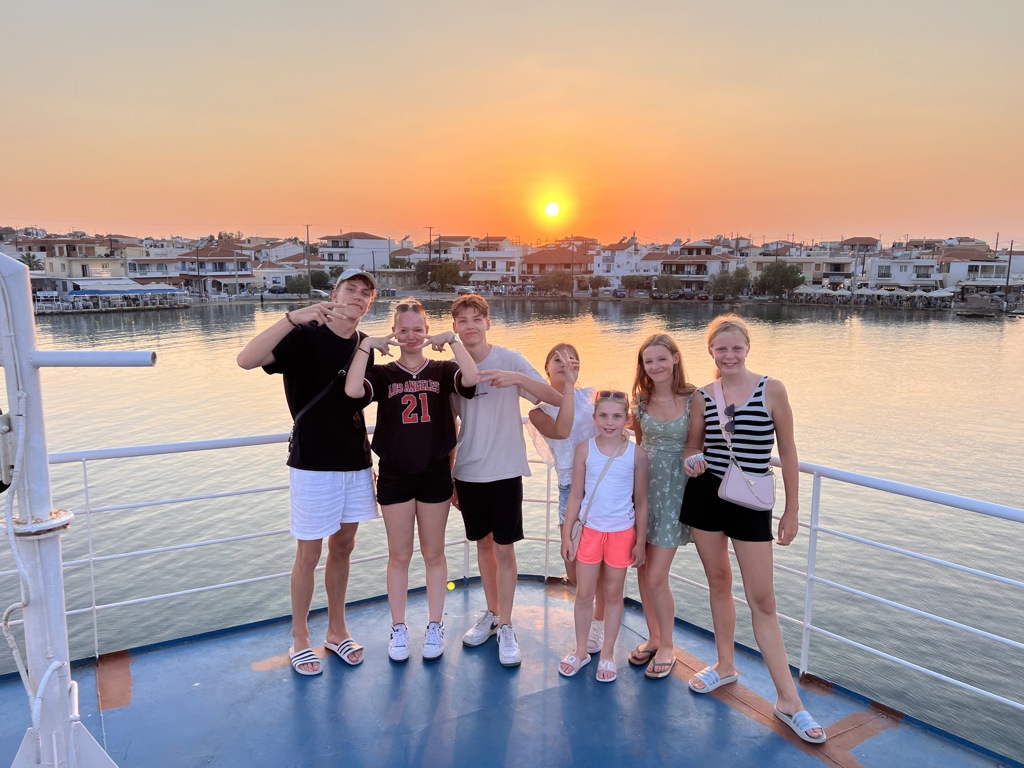 Gezin op boot bij zonsondergang in Noord-Griekenland, met haven en dorp op de achtergrond.