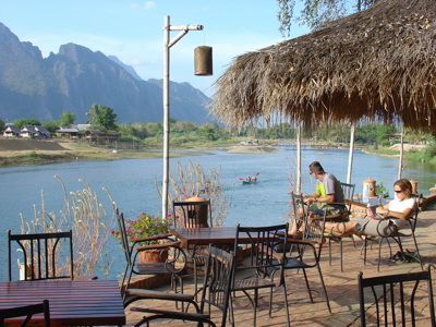 Terras aan de Nam Song-rivier in Vang Vieng, Laos, met uitzicht op karstbergen en kajakkers.