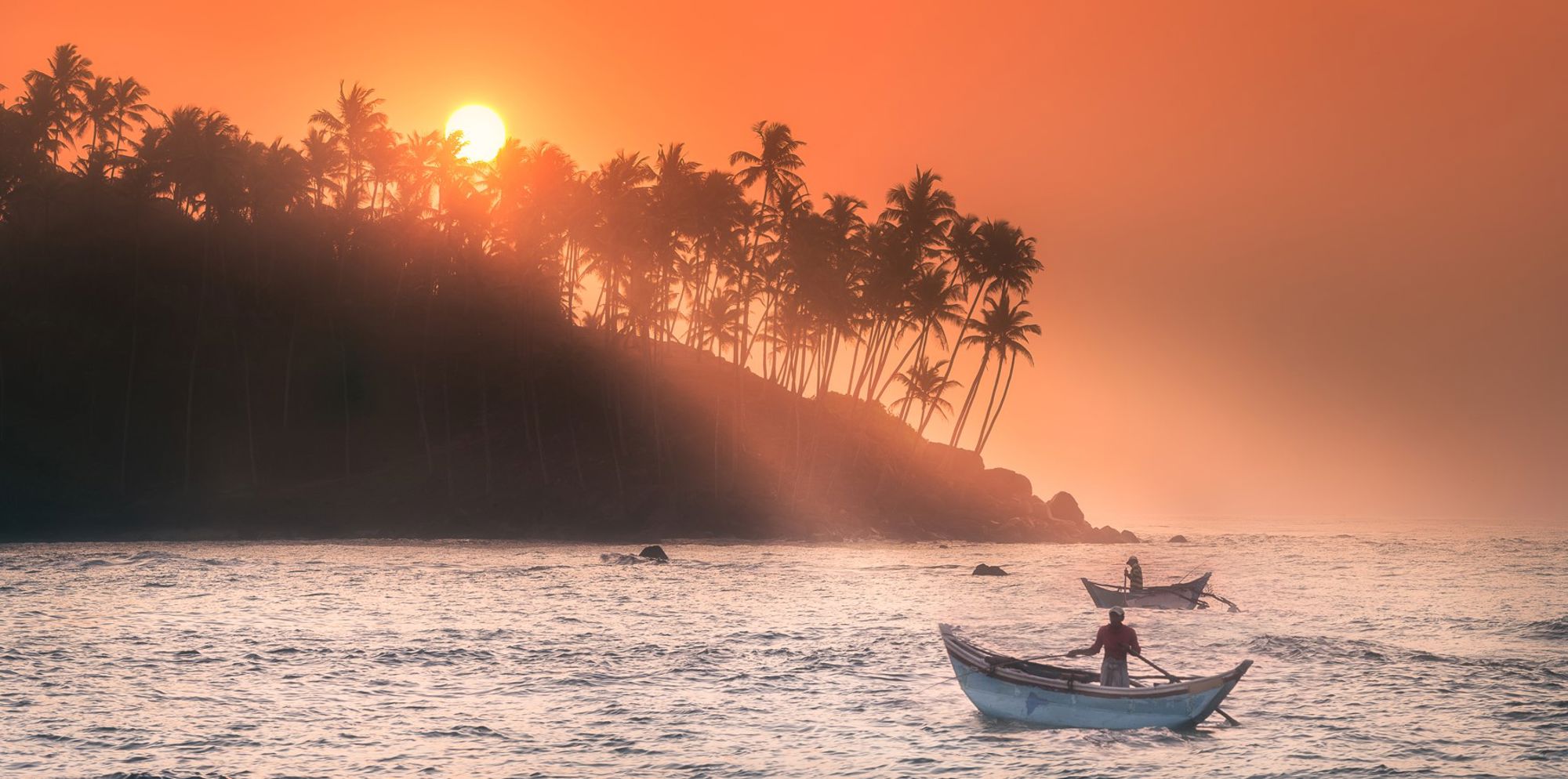 Vissers in bootjes op zee bij zonsondergang langs een palmenkust in Sri Lanka.