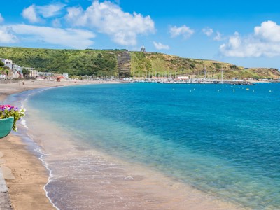 Strand en jachthaven van Praia da Vitória op Terceira, Azoren, met helderblauw water en groene heuvels.