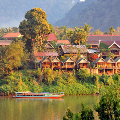 Rivierdorp met houten huisjes en boot bij zonsondergang tijdens familiereis Thailand, Laos en Cambodja.