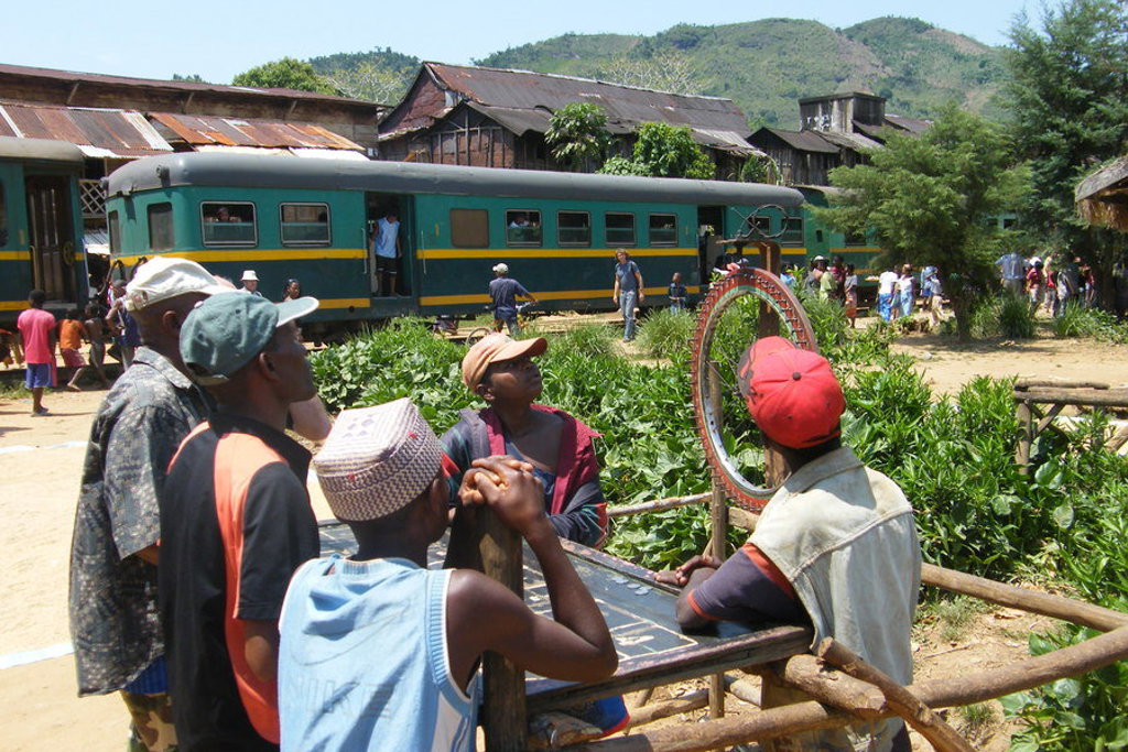 Lokale trein in Madagascar met reizigers op het perron en uitzicht op de heuvels.