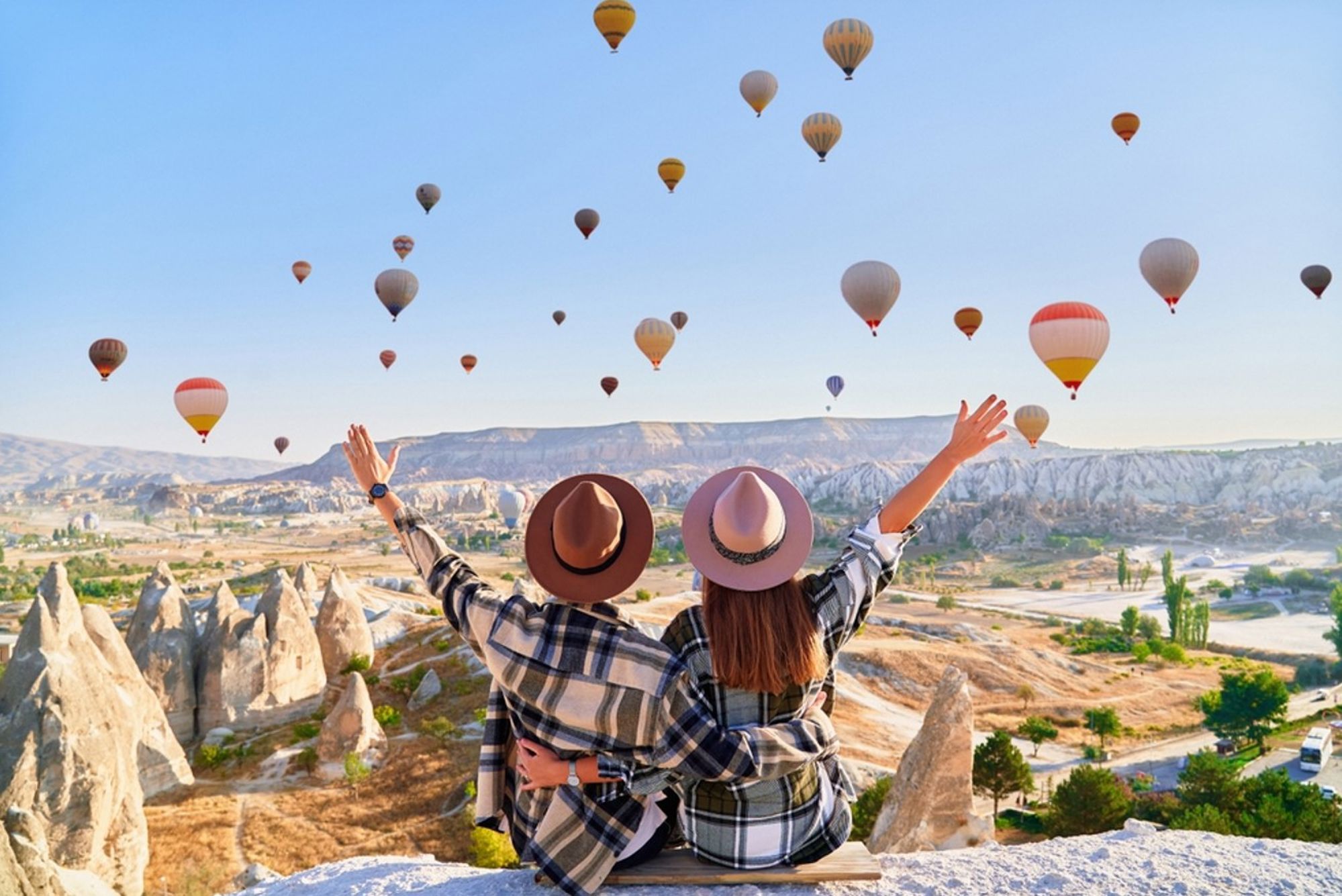 Twee reizigers kijken uit over Cappadocië in Turkije met tientallen luchtballonnen in de lucht.