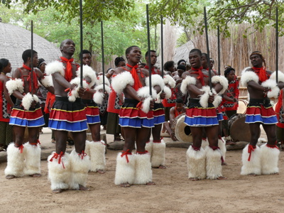 Traditionele dansgroep in Eswatini met kleurrijke kleding, speren en trommels tijdens Route Johannesburg - Kaapstad.
