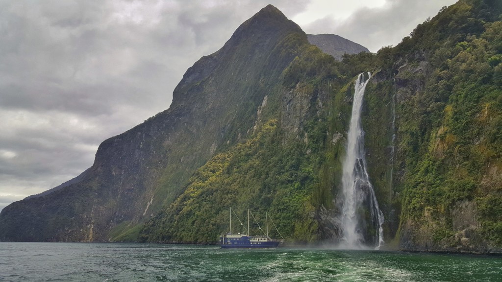 Cruiseboot bij waterval in Milford Sound, Nieuw-Zeeland, tijdens groepsrondreis door ruige natuur.