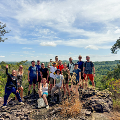 Groepsfoto van 22-35ers tijdens een hike met uitzicht over de groene heuvels van Thailand, Laos en Cambodja.