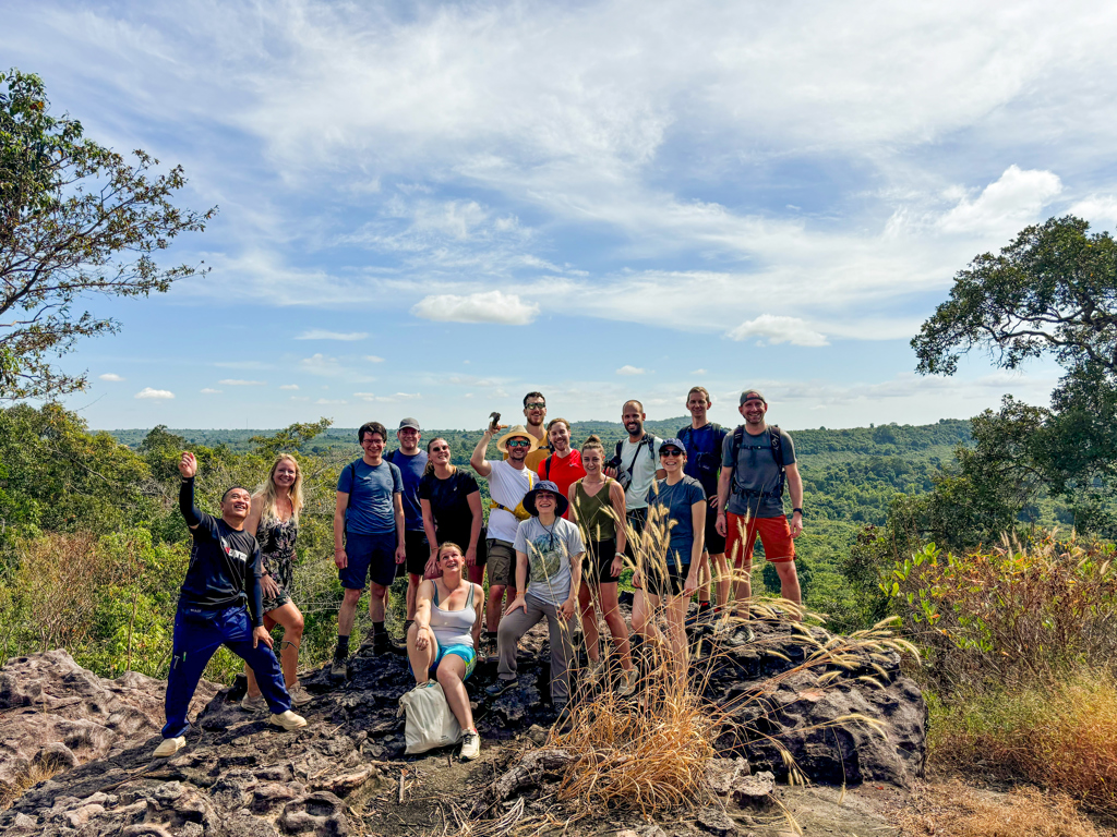 Groepsfoto van 22-35ers tijdens een hike met uitzicht over de groene heuvels van Thailand, Laos en Cambodja.