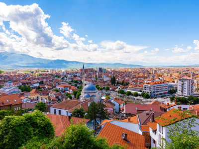 Panorama over Prizren in Kosovo met rode daken, moskee en bergen onder een blauwe lucht.
