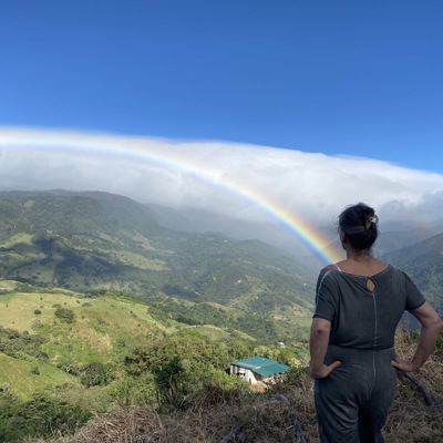Reiziger kijkt uit over groene bergen in Costa Rica met een regenboog boven de vallei.