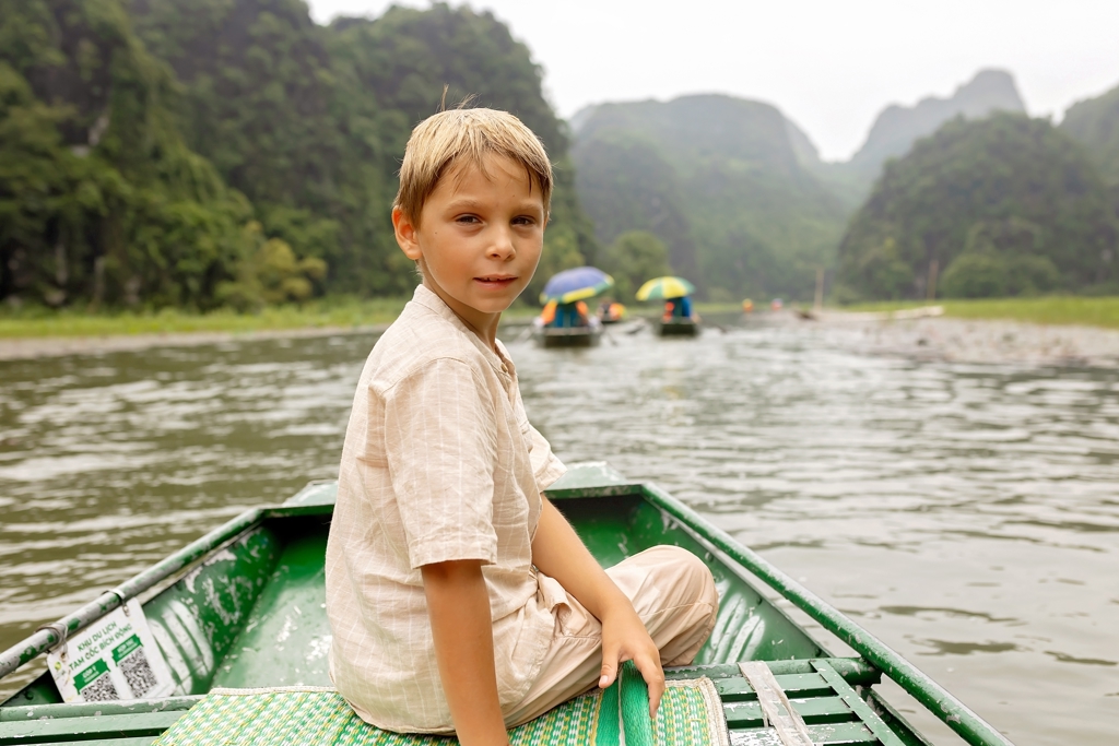 Jongen in roeiboot op rivier tussen groene kalksteenbergen tijdens familiereis Vietnam.