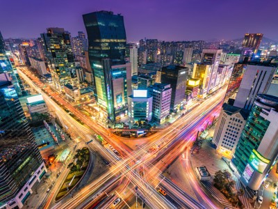 Avondzicht op Seoul met verlichte wolkenkrabbers en lichtstrepen van verkeer op een druk kruispunt.