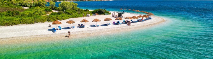 Strand van Agios Dimitrios met parasols en ligbedden aan helderblauw water, omringd door groene heuvels.